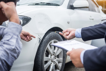 people holding clipboard and accident report next to damaged car